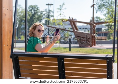 A happy attractive student girl in sunglasses taking a selfie photo on phone, chatting with friends on the street. A blogger girl using a smartphone for video communication. Video chat.