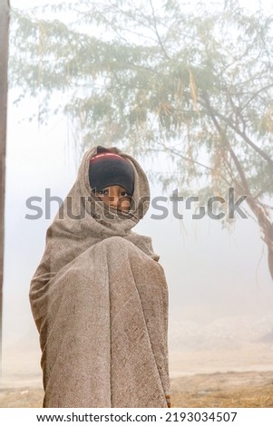 a homeless child is covering his body and face by a warm shawl in extreme cold weather  Royalty-Free Stock Photo #2193034507