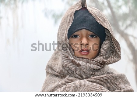 a homeless child is covering his body and face by a warm shawl in extreme cold weather  Royalty-Free Stock Photo #2193034509
