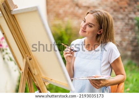 Woman enjoys painting on canvas outdoor.