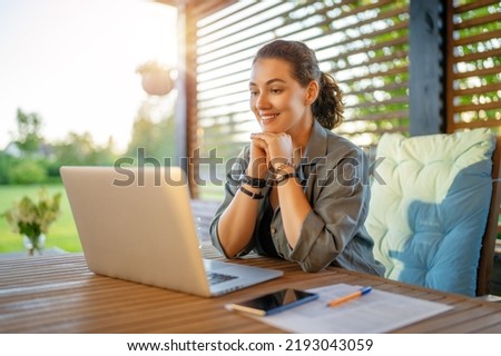 Happy young woman is working sitting on the patio in summer.