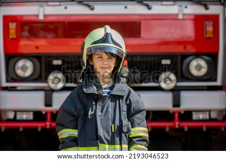Child, cute boy, dressed in fire fighers cloths in a fire station with fire truck, childs dream Royalty-Free Stock Photo #2193046523