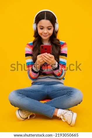 Teenager child holding cellphone. Close-up portrait of cute teen girl using mobile phone, cell web app, isolated over bright vivid vibrant yellow color background. Happy teenager, positive and