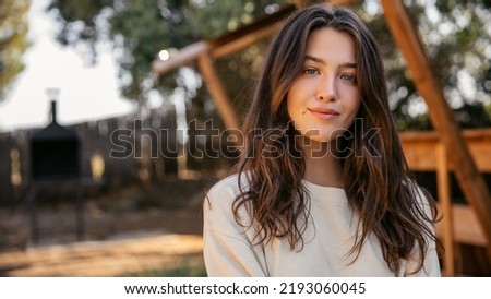 Close-up of pleasant young caucasian girl looking at camera relaxing outside city on weekend spring. Brunette woman with wavy hair wears sweatshirt on warm day. Lifestyle concept