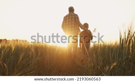 Farmer and his son in front of a sunset agricultural landscape. Man and a boy in a countryside field. Fatherhood, country life, farming and country lifestyle. Royalty-Free Stock Photo #2193060563