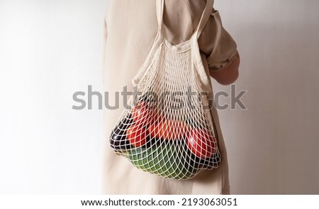 Reusable eco shopping bag. A girl in a cotton dress holds a reusable mesh bag with fresh vegetables. Zero waste, care for the environment, no plastic concept. Royalty-Free Stock Photo #2193063051