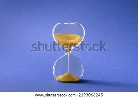 Hourglass, also known as sandglass or sand timer. Single glass sand clock with golden sand on blue paper background. Design element, Royalty-Free Stock Photo #2193066245