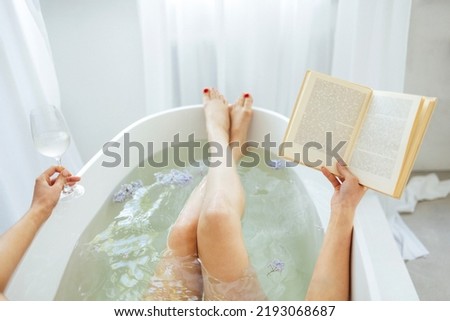 Back view of the young brunette woman reading the book and drinking white wine in bath with foam and candles Royalty-Free Stock Photo #2193068687