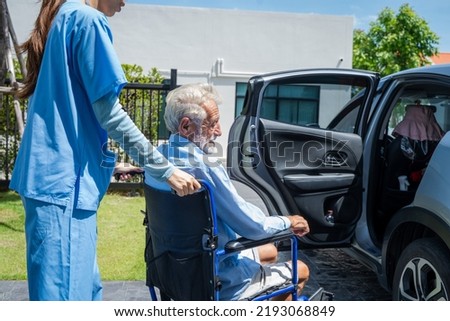 Nurse takes care of a disabled senior man in a wheelchair into a car to take him to the hospital for a check-up.