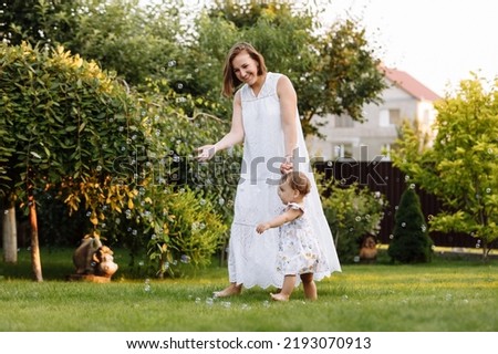 Happy Mothers Day. Young smiling mother with adorable baby daughter is having fun on backyard on summer day. Family holiday in garden. Mum and child girl walking on nature. Happy childhood. Family day