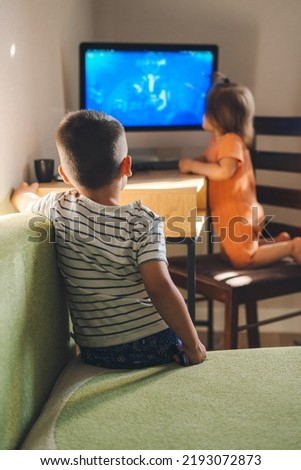 Rear view of a boy sitting on the sofa watching a cartoon on the computer with his sister. Modern technology. Children smart technology gadget usage concept Royalty-Free Stock Photo #2193072873
