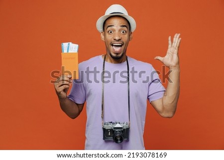 Traveler black man wear purple t-shirt hat hold pasport ticket spread hand isolated on plain orange color background. Tourist travel abroad in spare time rest getaway. Air flight trip journey concept Royalty-Free Stock Photo #2193078169