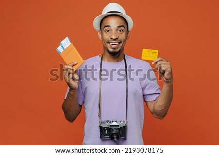 Traveler black man wear purple t-shirt hat hold passport credit card isolated on plain orange color background Tourist travel abroad on weekends spare time rest getaway Air flight trip journey concept