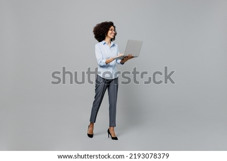 Full body fun successful young employee business corporate lawyer woman of African American ethnicity in classic formal shirt at office hold use work on laptop pc computer isolated on grey background