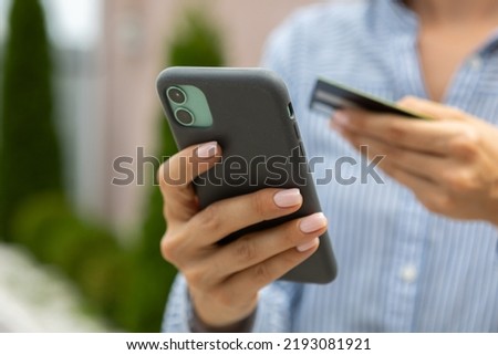 female hands hold a modern mobile phone and a bank credit or debit card on the street.
ordering purchases, working online, transferring money by phone through a mobile application