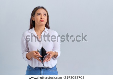 Unhappy young Asian woman holding empty wallet and looking away at copy space isolated over white background Royalty-Free Stock Photo #2193083705