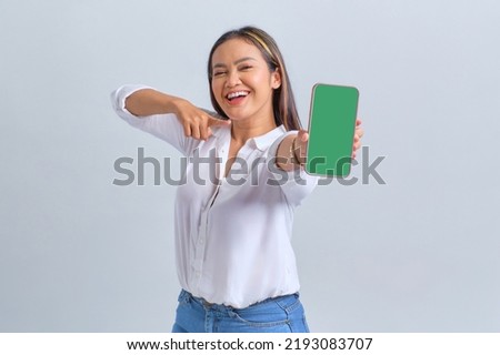 Excited young Asian woman showing blank screen mobile phone, recommending mobile app isolated over white background