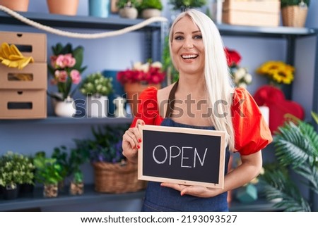 Caucasian woman working at florist holding open sign smiling and laughing hard out loud because funny crazy joke. 