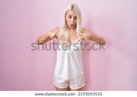 Caucasian woman wearing pajama wearing pink background pointing down with fingers showing advertisement, surprised face and open mouth 