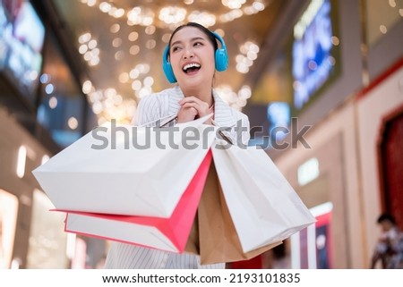 Smiling asian woman hold shopping bags listening music headphone. Young woman relax shopping in shopping mall Purchases, black friday, discounts, sale concept. Online shopping concept.