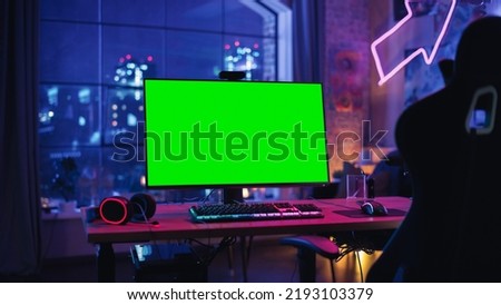 Gaming at Home: Empty Gaming Station with Player's Personal Computer with Green Screen Chroma Key Display Standing on a Wooden Desk in Stylish Loft Apartment with Neon Lights.