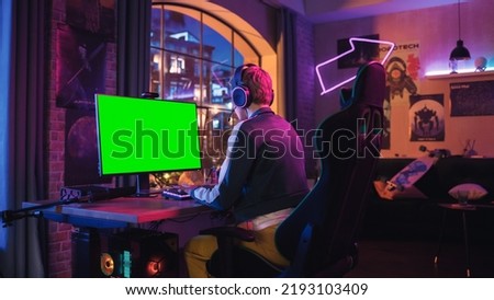 Attractive Female Gamer Playing Online Video Game with a Mock Up Green Screen on Her Powerful Computer. Room and PC have Colorful Neon Led Lights. Fun Evening at Home in Modern Apartment.