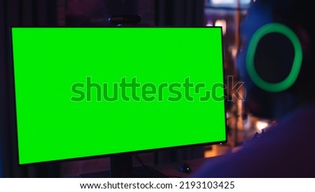 Excited Black Gamer Playing Online Video Game with a Mock Up Green Screen on His Powerful Personal Computer. Room and PC have Colorful Neon Led Lights. Cozy Evening at Home in Stylish Apartment.