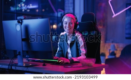 Portrait of a Female Gamer Playing Online Video Game on Computer. Stylish Young Woman with Short Hair in Headphones Enjoying Leisure Time, Smiling and Posing for Camera. Cyber Gaming Neon Room.