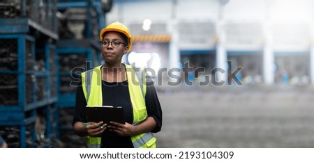 Plus size black female worker wearing safety hard hat helmet inspecting old car parts stock while working in automobile large warehouse