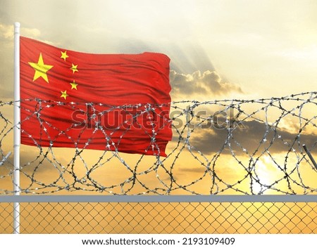 Flagpole with the flag of China against the sky and behind a fence with barbed wire. The concept of protecting the borders of territories.