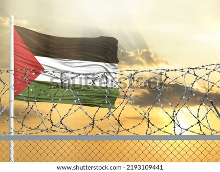 Flagpole with the flag of Palestine against the sky and behind a fence with barbed wire. The concept of protecting the borders of territories.