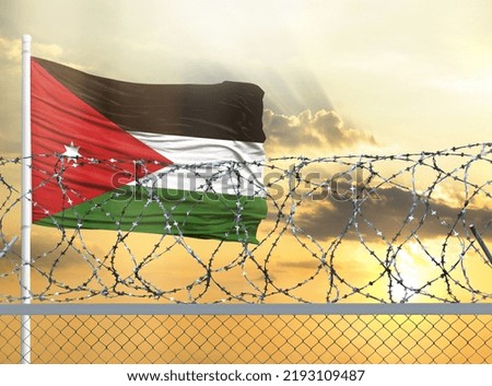 Flagpole with the flag of Jordan against the sky and behind a fence with barbed wire. The concept of protecting the borders of territories.