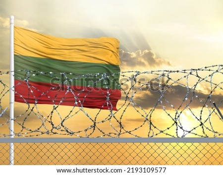 Flagpole with the flag of Lithuania against the sky and behind a fence with barbed wire. The concept of protecting the borders of territories.