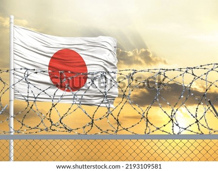 Flagpole with the flag of Japan against the sky and behind a fence with barbed wire. The concept of protecting the borders of territories.