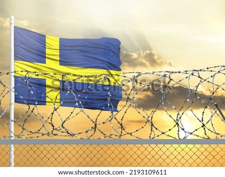 Flagpole with the flag of Sweden against the sky and behind a fence with barbed wire. The concept of protecting the borders of territories.