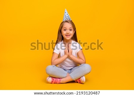Full length photo of charming excited school girl wear white t-shirt birthday cap sitting floor isolated yellow color background