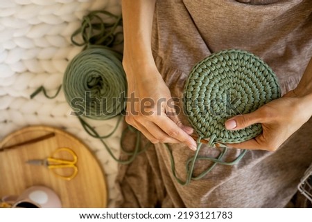 Closeup female hands knitting interior decor basket use green ribbon yarn and crochet needle. Creative woman arms enjoying needlecraft hobby or art work making comfortable cotton sewing accessories Royalty-Free Stock Photo #2193121783