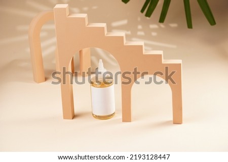 A mock-up of a transparent cosmetics bottle with yellow liquid and white label in peach colored arched doors for cosmetics photography on beige colored background