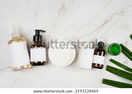 A mock-up of a brown cosmetics bottle with dispenser and white label, round cream container, bottle with pipette on marble background lined up and green palm leaf, top view