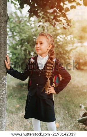back to school. little happy kid pupil schoolgirl eight years old in fashion uniform with backpack and hairstyle voluminous long braid ready going to second grade first day at primary school. flare Royalty-Free Stock Photo #2193142019
