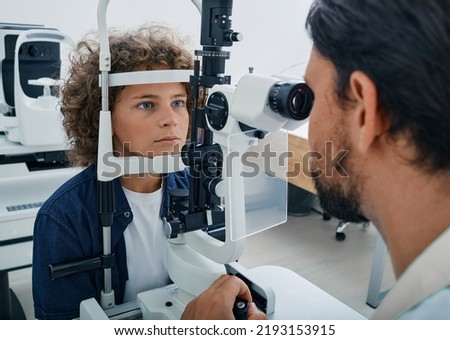 Curly boy getting eye exam at ophthalmology clinic with optometrist. Checking retina of male child eye, ophthalmology for children Royalty-Free Stock Photo #2193153915