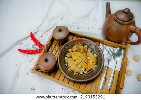picture of pempek, a typical food from the city of Palembang, Indonesia, served on a clay plate with a teapot and clay glass, on white background.