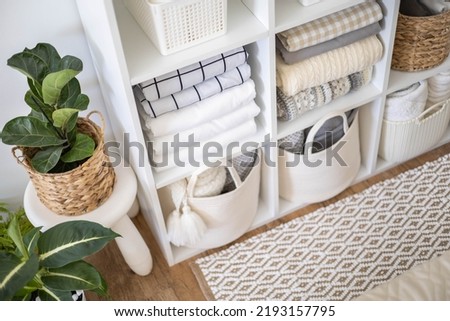 Neatly folded linen cupboard shelves storage at eco friendly straw basket placed closet organizer drawer divider. Stacks towels pillows plaids soft sheets bedding cabinet filling Nordic organization Royalty-Free Stock Photo #2193157795