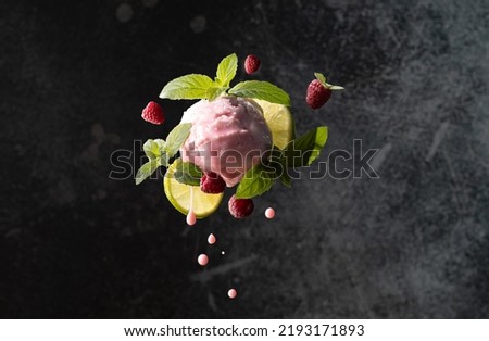 Flying raspberry ice cream scoop with fresh ripe berries,lime slices,mint leaves and falling drops on black background.Close up of ice cream in freeze motion. Royalty-Free Stock Photo #2193171893