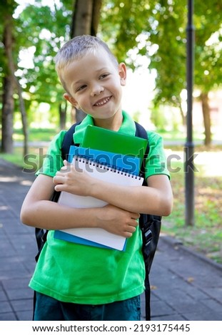 Back to school. a elementary school student. First grader. The beginning of classes. A child boy with a backpack holds textbooks and a notebook in his hands and smiles
