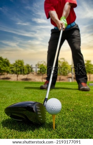 An extreme closeup of the golf driver and ball on the grass with a golfer ready to swing the driver. driver close-up view. selective focus golf driver and out of focus golfer. shot of golf club Royalty-Free Stock Photo #2193177091