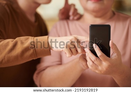 Closeup image of teenage boy explaining grandmother how to use social media application on smartphone