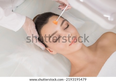 Cosmetic procedure. Chemical peeling. Doctor's hand with a brush touching the face of a young beautiful woman. Facial skin care. Place for text. Royalty-Free Stock Photo #2193195479