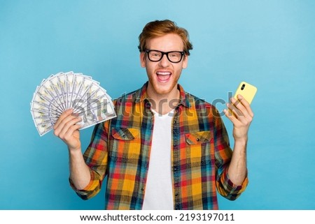 Photo of excited satisfied positive guy with red hair dressed plaid shirt win on bets lots of money isolated on blue color background