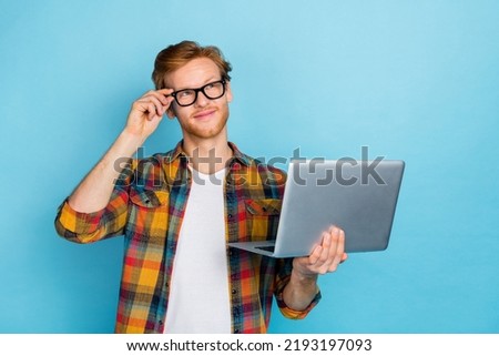 Photo of smart handsome thoughtful guy with red hair wear plaid shirt hold laptop arm on glasses isolated on blue color background